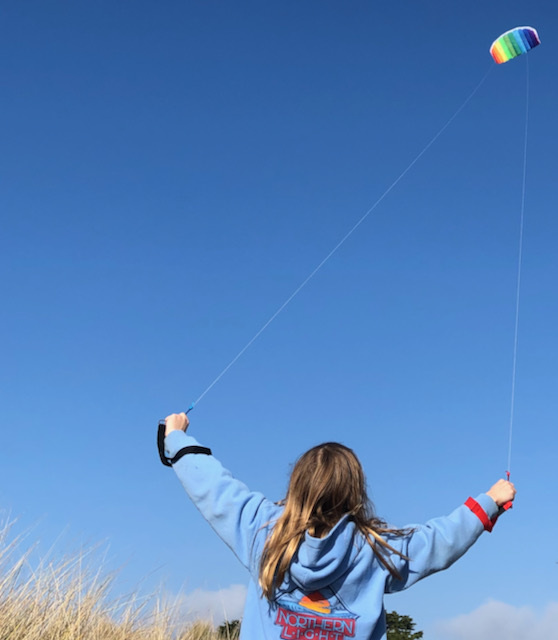 young person flying a kite where the parallel kite strings appear to come together when they reach the kite in the distance